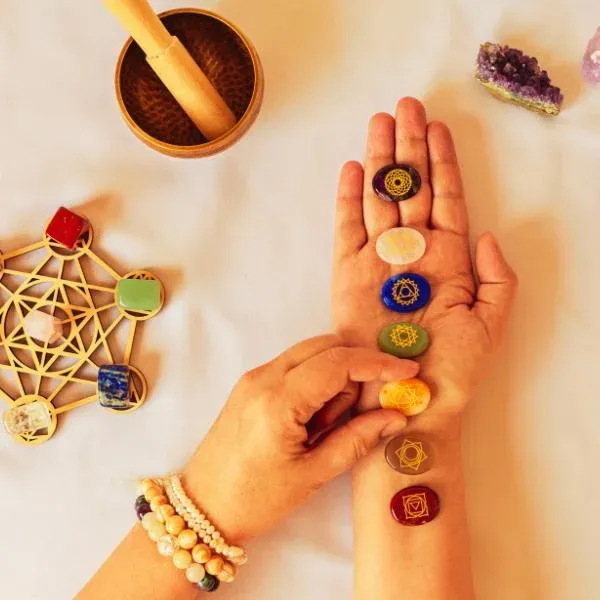 Main tendue portant les sept pierres des chakras, bol chantant et cristaux